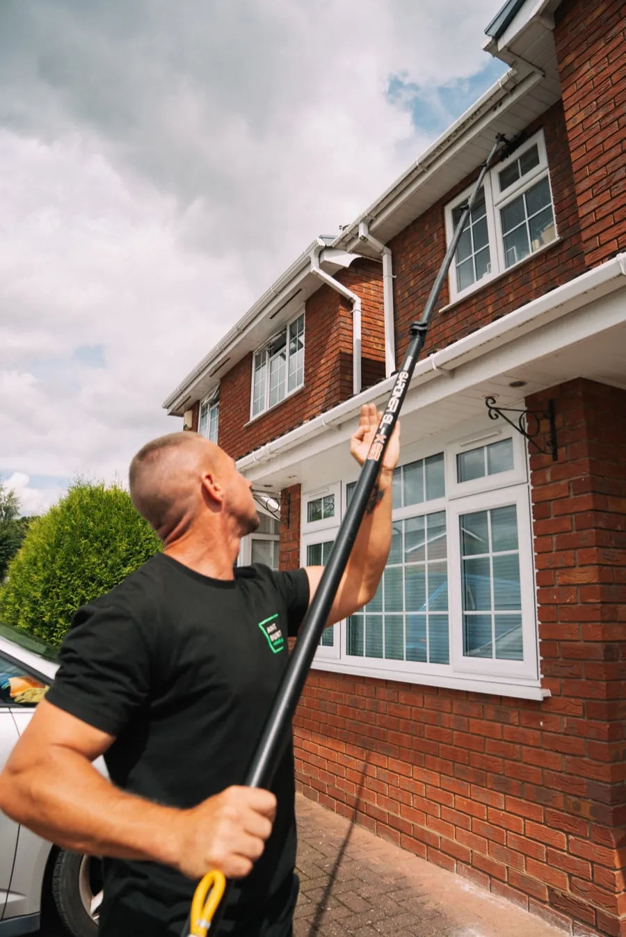Ant cleaning the upstairs windows of a red-brick Tamworth home with a water-fed pole from the ground