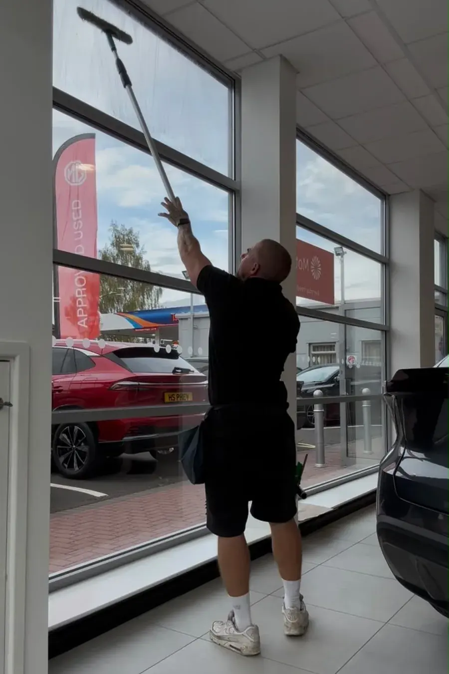 Ant Burton cleaning the inside of the showroom glass at Polesworth Garage with a traditional applicator on an extension pole, worked from the floor